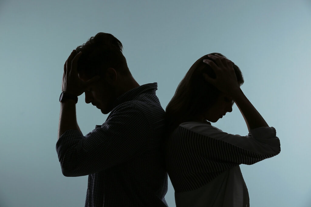 two people in the dark hold their forehead while struggling with the idea of codependency and addiction