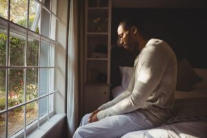 man sits near a window and looks out while appearing distraught while thinking about the effects of heroin overdose symptoms