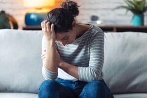woman holds her palm to her head while sitting on a couch and struggling with cocaine side effects