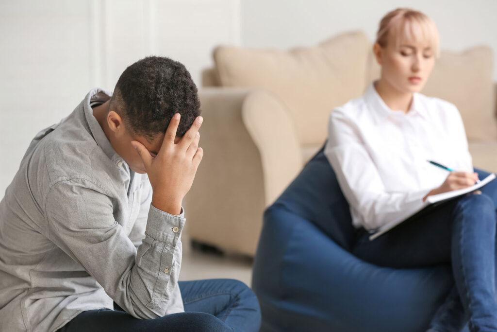 a man struggling with symptoms of heroin withdrawal sits and holds his head with his hand while in a session with his addiction specialist