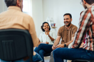 a group of people sit together in a circle and are laughing and talking about how important addiction support groups have been for them