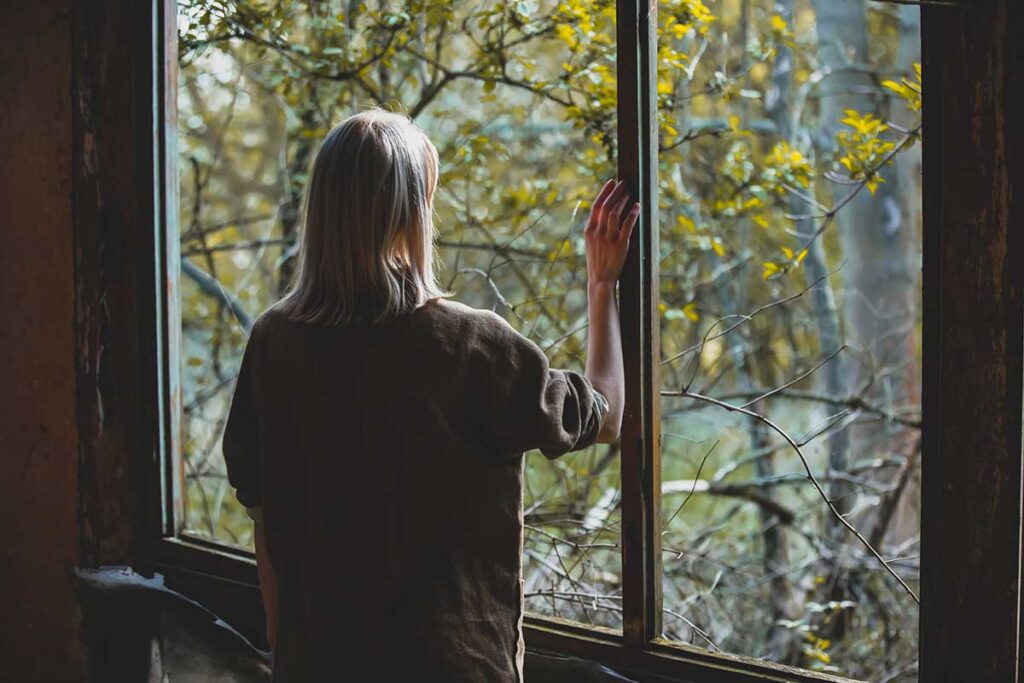 person stands by window hold hand on window and wondering if quitting alcohol cold turkey​ is safe