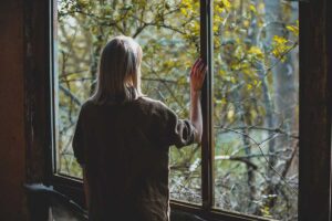 person stands by window hold hand on window and wondering if quitting alcohol cold turkey​ is safe