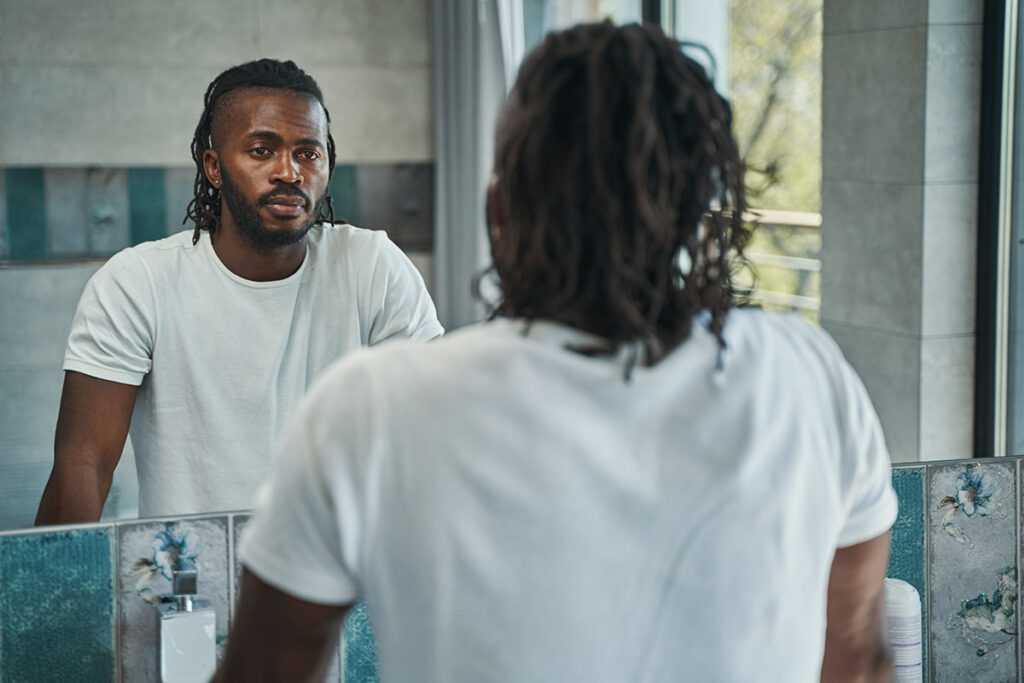 a man stares at his reflection in a mirror and thinks about his self destructive behaviors