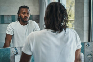 a man stares at his reflection in a mirror and thinks about his self destructive behaviors