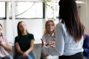 a woman speaks to a group and answers one of the group members question of can I work while in rehab