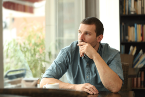 man holds his hand to his mouth while looking out a window thinking about benzo withdrawal symptoms