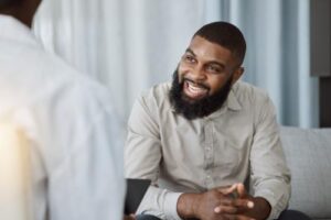 a man sits on a couch talking to his therapist and smiles during his alcohol addiction treatment