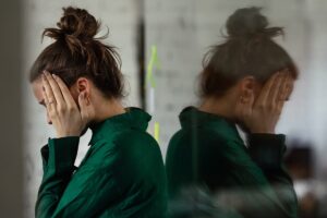 an upset woman leans against a mirror while holding her hands to the side of her face distraught over the most commonly abused painkillers