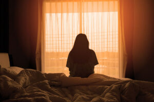 person sits at the edge of their bed in a dark bedroom and thinks about an alcoholics life expectancy