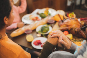 a group of people holding hands sitting at a table with thanksgiving dinner celebrate a sober thanksgiving