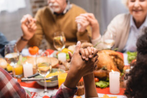 a family holds hands at a dinner table with food on the table while experiencing the holidays while in recovery