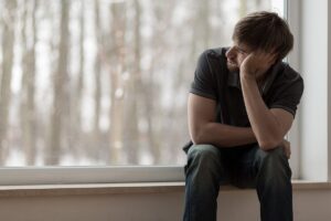 man sits near a window and looks out while struggling with the signs of ptsd