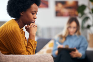 a woman sits on a couch thinking about how long is vivitrol treatment while her therapist sits in the background taking notes on clipboard