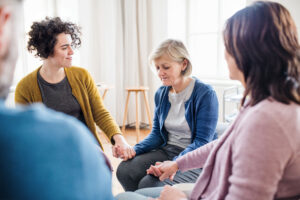 a group of women sit around and holds hands experiencing a deep connection with others which is one of many benefits of a women's rehab