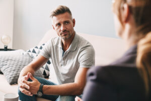 older male sits on a couch and listens to his therapist discuss the options for medication for alcohol withdrawal