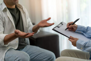 a person talks with their hands while a therapist makes note on their clipboard about ptsd treatment programs and benefits for the patient