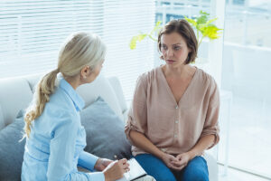 woman sits on a couch with her hands in her lap while asking what are the 12 steps of aa to her therapist