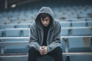an adult male wearing a hoodie sits outside in bleachers wondering what the signs of xanax addiction are