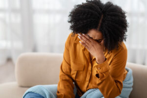 an upset woman holds her hand to her forehead while leaning over and struggling with some of the signs of prescription drug abuse