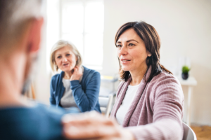 a woman with brown hair holds the shoulder of the person next to her while discussing benefits of addiction treatment programs