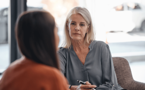 a older adult woman sits and listens to someone talking about inpatient addiction treatment