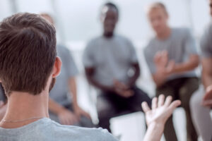 a man sits with a group and talks about how alcoholics anonymous meetings have helped with his recovery