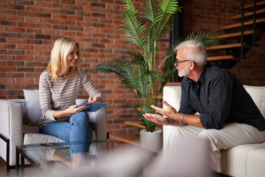 blond woman sits on a couch while talking to her sponsor in her faith based recovery programs