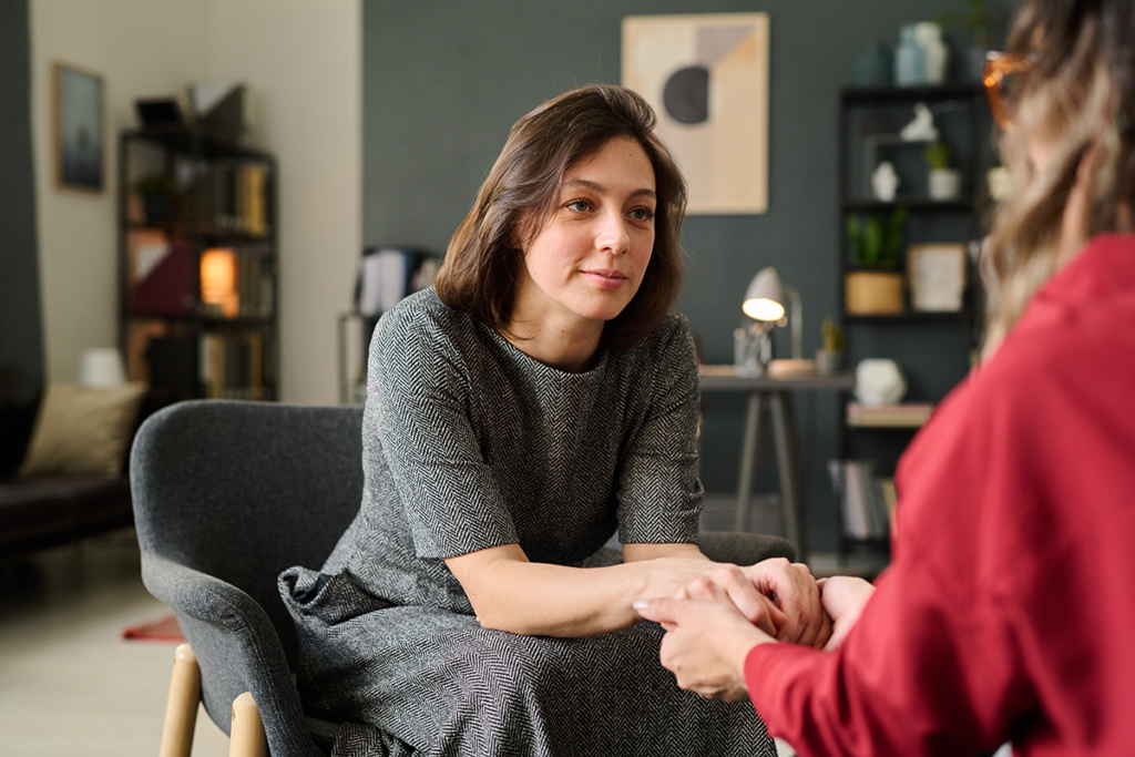 a woman sits and leans towards another person while making amends in recovery