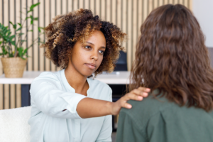 a woman puts her hand on another womans shoulder after discussing benefits of medication assisted treatment 