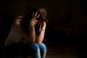 distraught woman sits in the dark with hand to her head wondering why do people with ptsd develop substance abuse